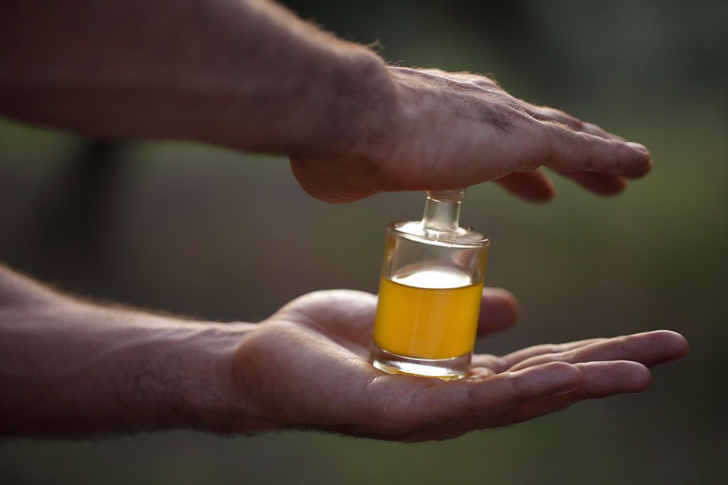 Hände halten eine kleine Glasflasche naturtrübes Olivenöl